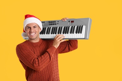 Photo of Man in Santa hat playing synthesizer on yellow background. Christmas music