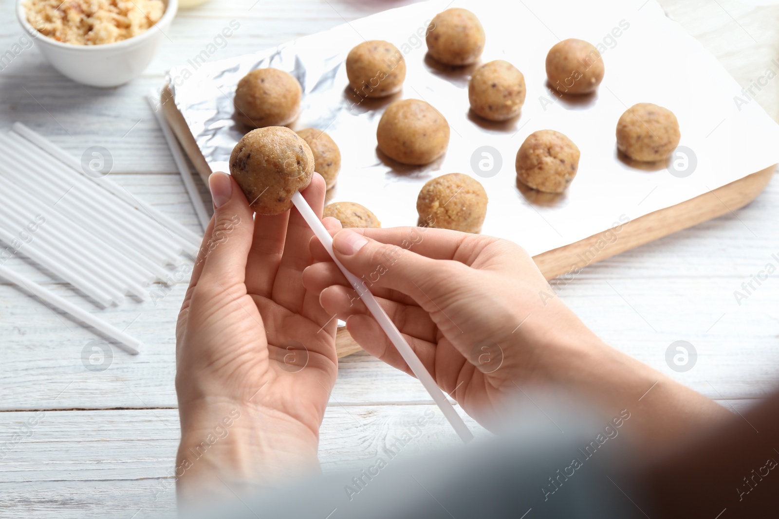 Photo of Woman making tasty cake pops at white wooden table, closeup