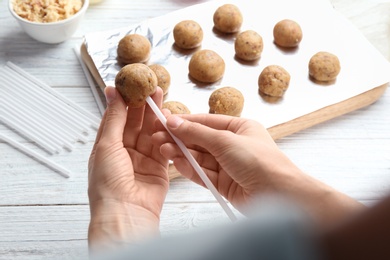 Woman making tasty cake pops at white wooden table, closeup