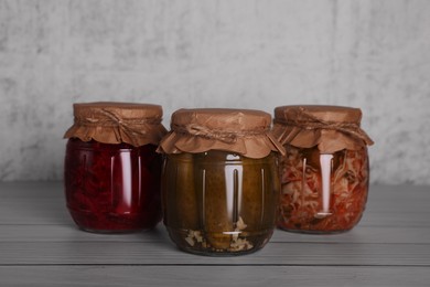 Glass jars with different preserved vegetables on wooden table