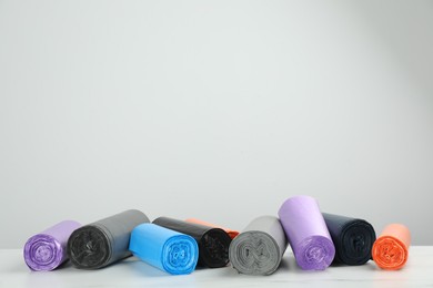 Rolls of different color garbage bags on table against light background. Space for text