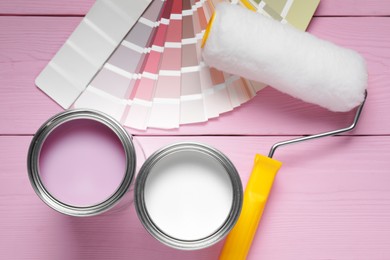 Cans of pink and white paints, roller with palette on color wooden table, flat lay