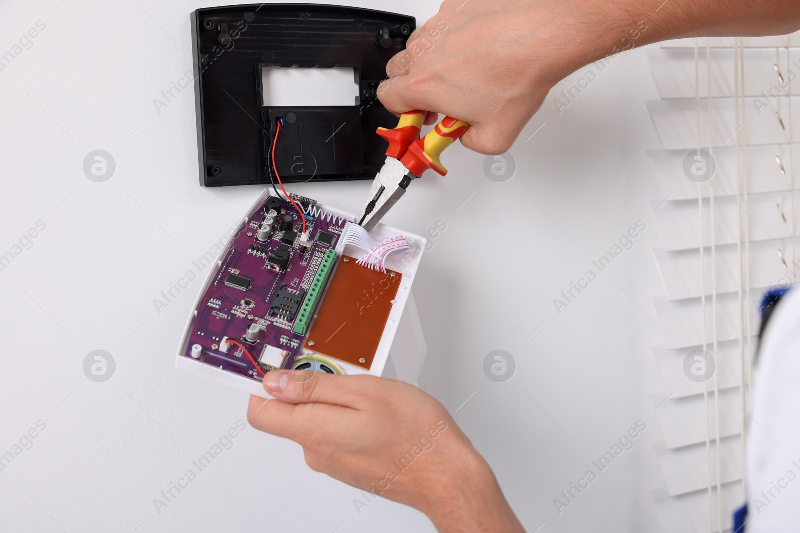 Photo of Man installing home security alarm system on white wall indoors, closeup