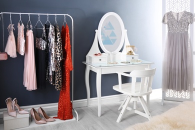 Photo of Rack with collection of beautiful festive clothes and dressing table in stylish room interior