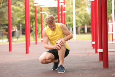 Young man suffering from knee pain on sports ground