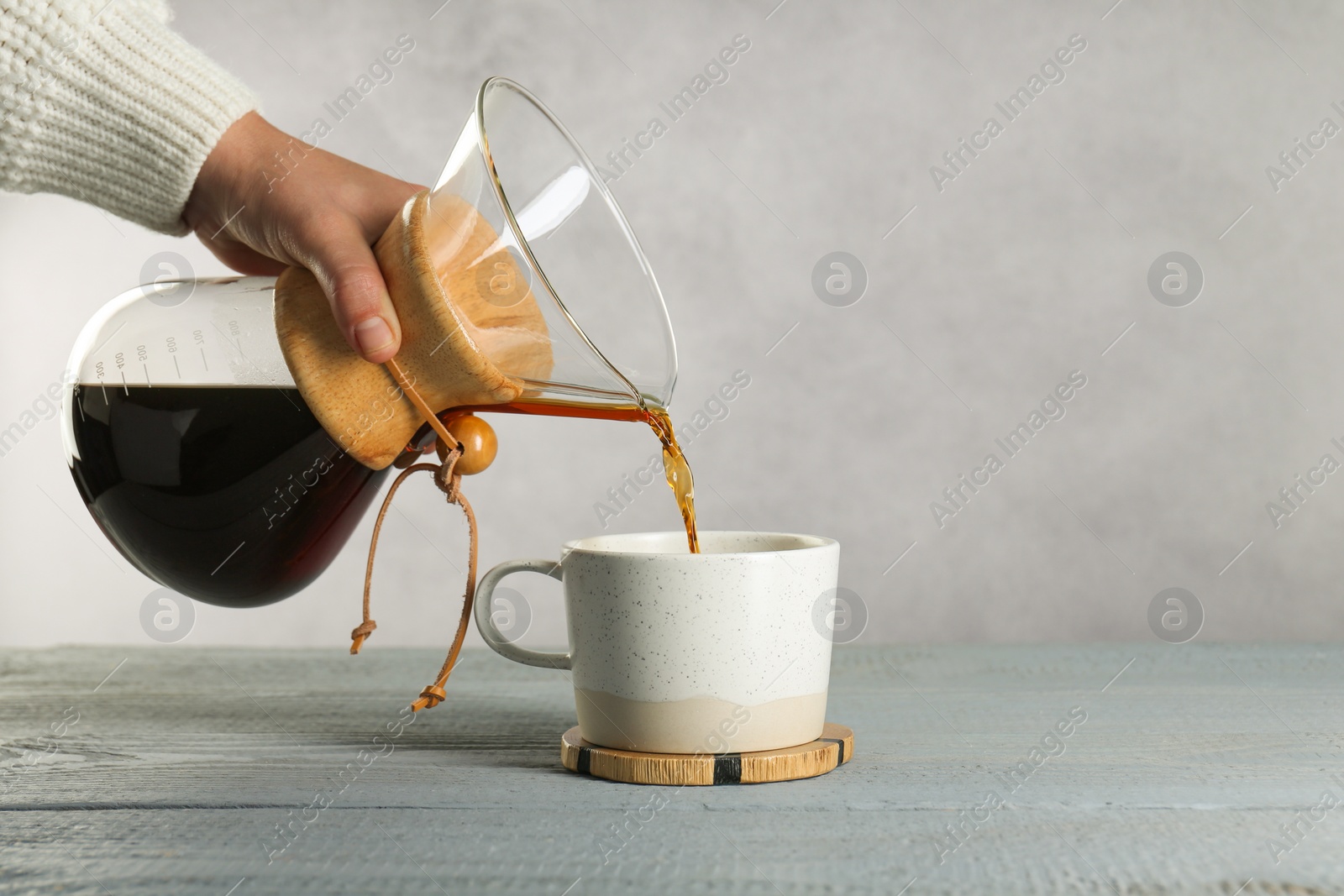 Photo of Woman pouring tasty drip coffee into cup at grey wooden table, closeup. Space for text