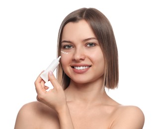 Young woman applying cream under eyes on white background