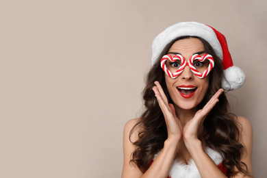 Emotional woman in Christmas costume with party glasses on beige background, space for text