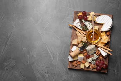 Photo of Cheese plate with honey, grapes and nuts on grey table, top view. Space for text