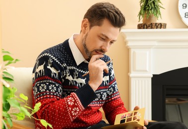 Photo of Man writing wishes in Christmas greeting card in living room