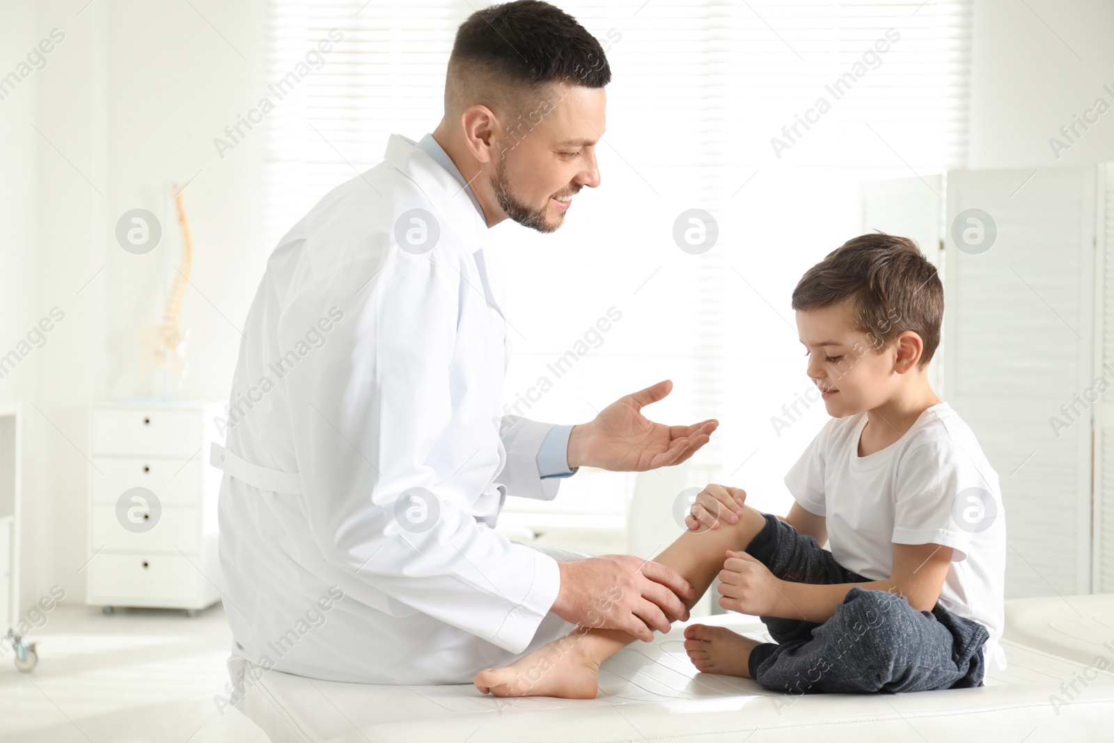 Photo of Professional orthopedist examining little patient's leg in clinic