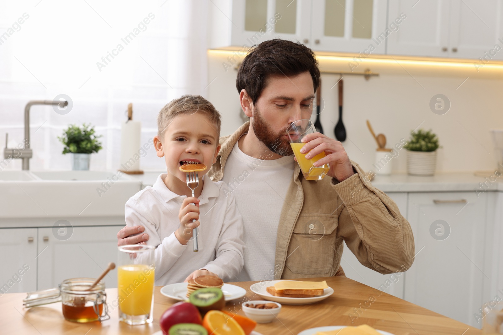 Photo of Father and his cute little son having breakfast at table in kitchen