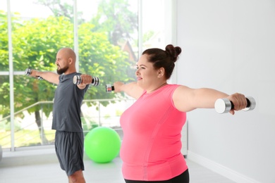 Overweight man and woman doing exercise with dumbbells in gym