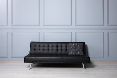 Stylish leather sofa near white wall in room. Interior design