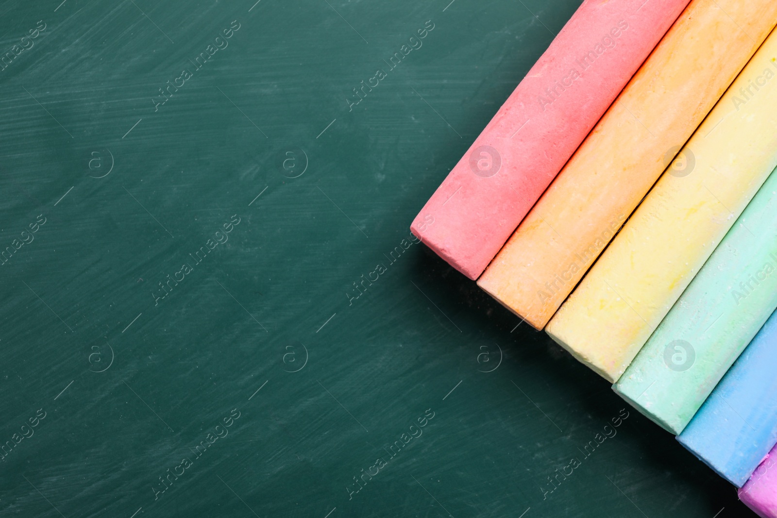 Photo of Pieces of color chalk on greenboard, flat lay. Space for text