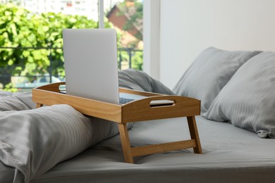 Photo of Wooden tray table with laptop on bed indoors