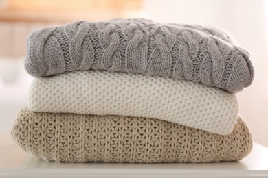Stack of folded warm sweaters on white table indoors, closeup