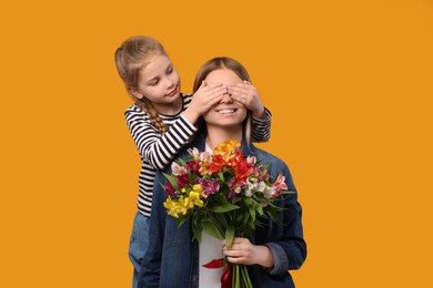 Photo of Little daughter congratulating her mom with flowers on orange background. Happy Mother's Day