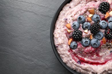 Photo of Tasty oatmeal porridge with toppings in bowl on dark table, top view. Space for text