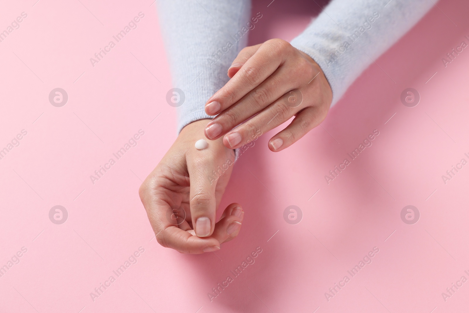 Photo of Woman applying cosmetic cream onto hand on pink background, closeup