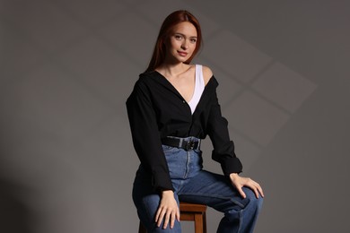 Photo of Beautiful young woman sitting on stool against gray background