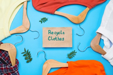 Photo of Different clothes with recycling label and hangers on light blue background, flat lay