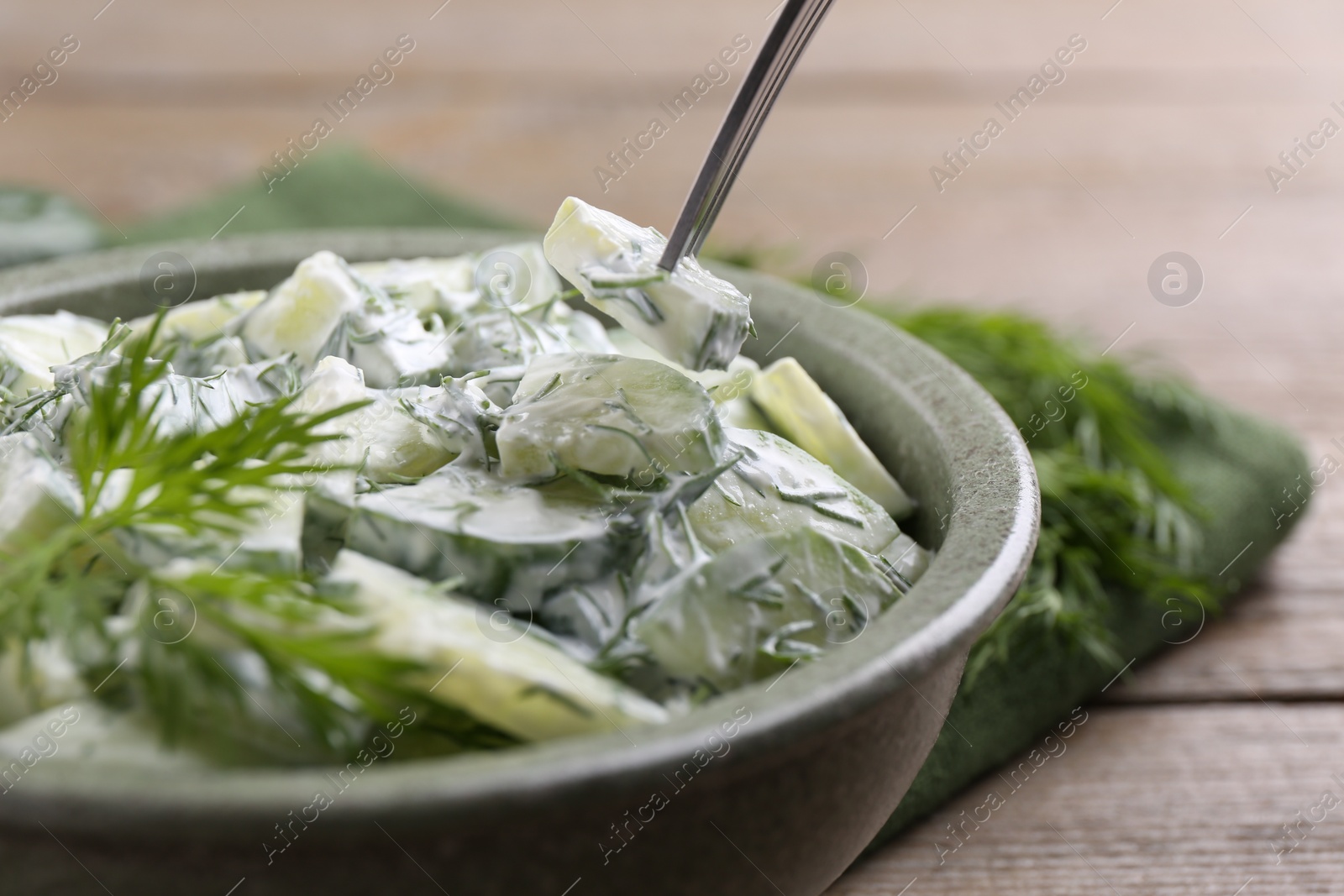 Photo of Eating delicious cucumber salad at wooden table, closeup
