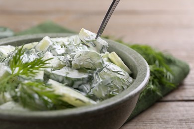 Eating delicious cucumber salad at wooden table, closeup