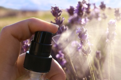 Photo of Woman spraying facial toner with lavender essential oil out of bottle in blooming field, closeup
