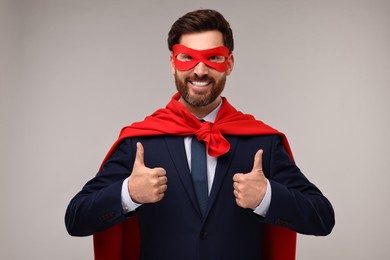 Photo of Happy businessman in red superhero cape and mask showing thumbs up on beige background