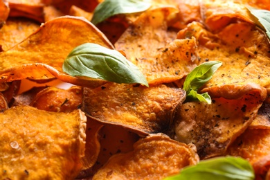 Photo of Sweet potato chips with basil as background, closeup