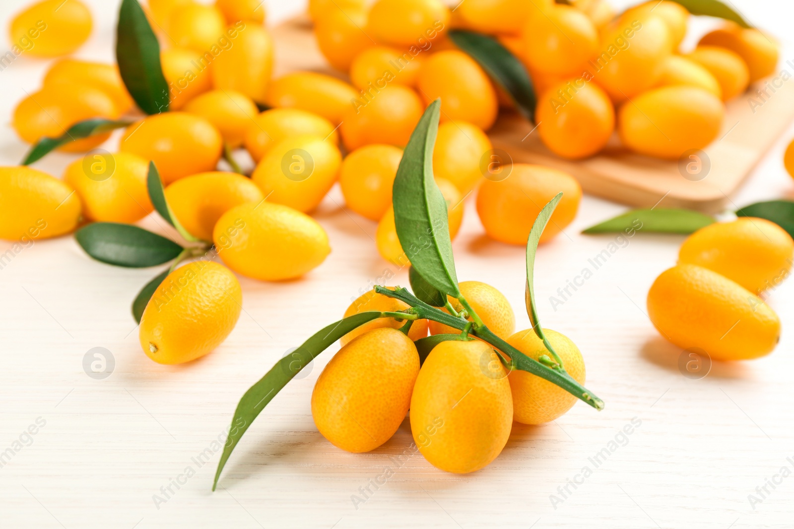 Photo of Fresh ripe kumquats with green leaves on white wooden table