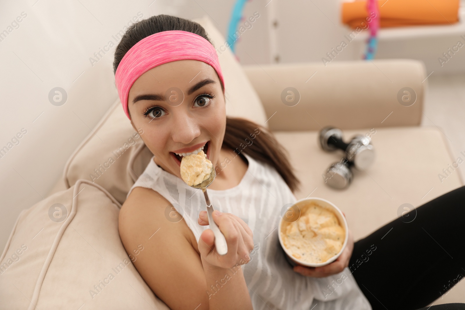 Photo of Lazy young woman eating ice cream instead of training at home