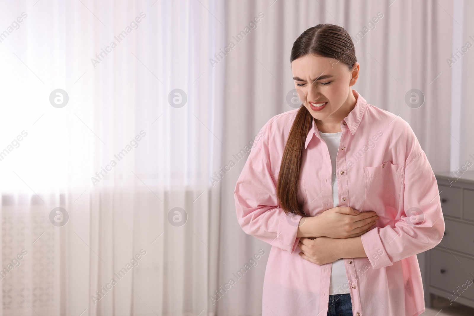 Photo of Young woman suffering from stomach pain at home. Space for text