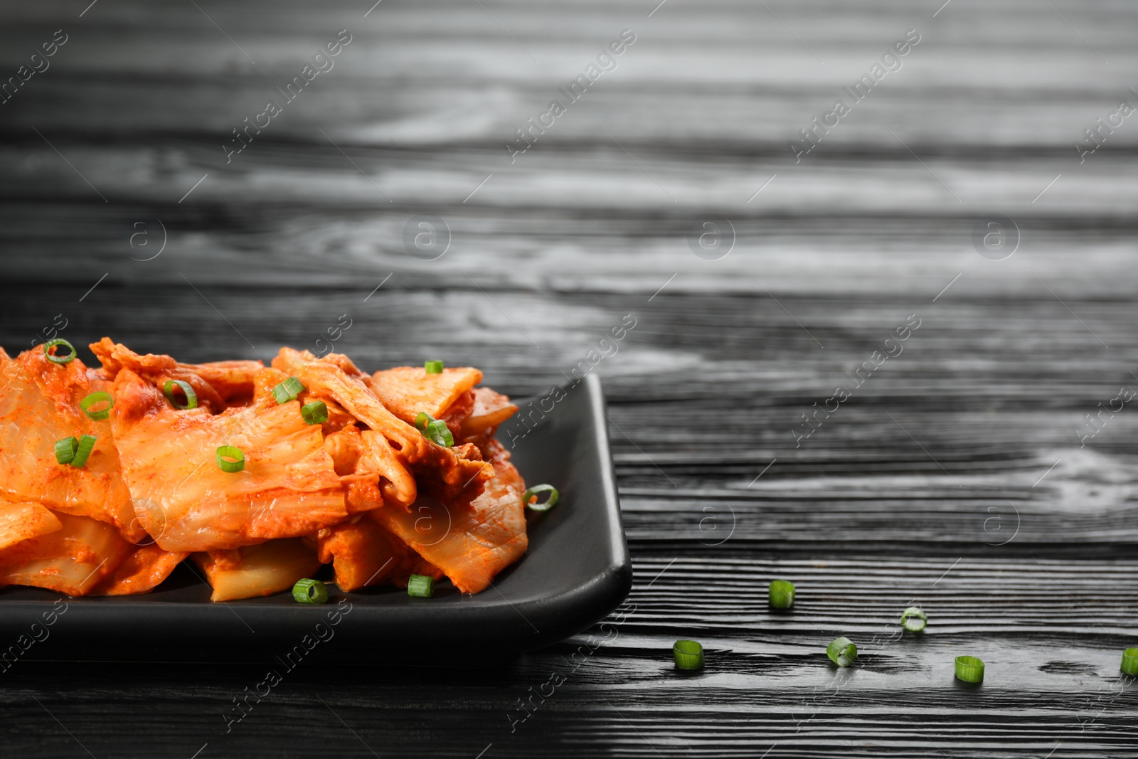 Photo of Delicious kimchi with Chinese cabbage and green onions on black wooden table, space for text