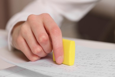 Photo of Girl erasing mistake in her notebook at white desk, closeup