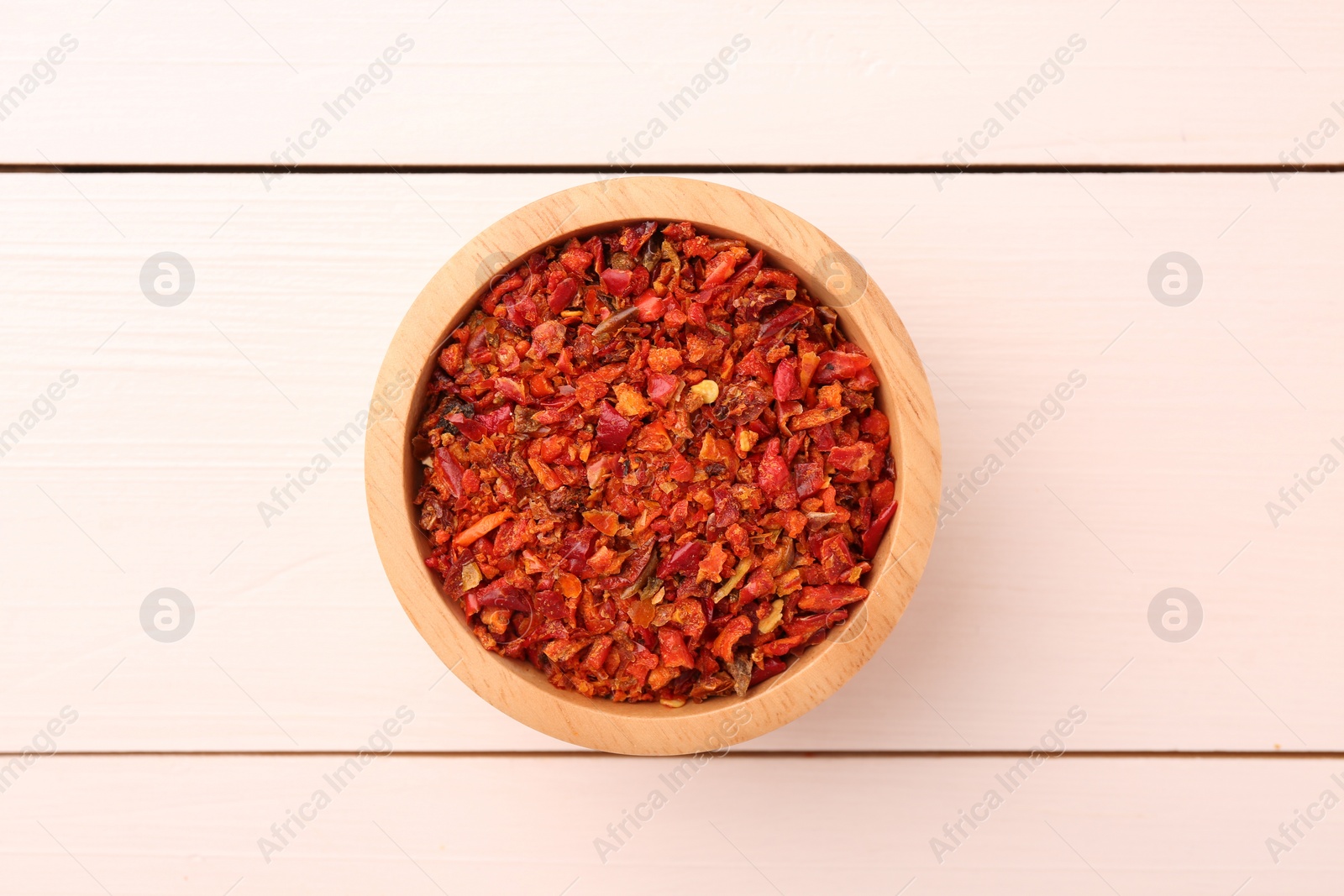 Photo of Chili pepper flakes in bowl on white wooden table, top view