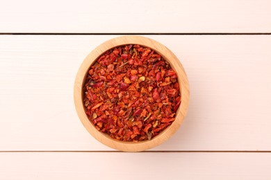 Photo of Chili pepper flakes in bowl on white wooden table, top view