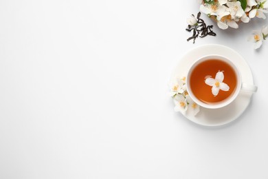 Cup of aromatic jasmine tea and fresh flowers on white background, top view. Space for text