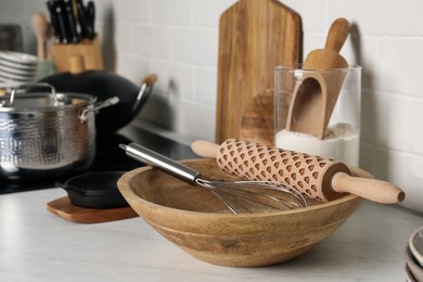 Photo of Wooden bowl with rolling pin and whisk on countertop in kitchen, closeup. Cooking utensils