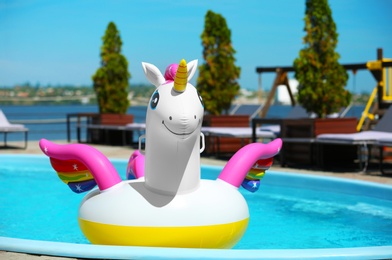 Funny inflatable unicorn ring floating in swimming pool on sunny day, outdoors