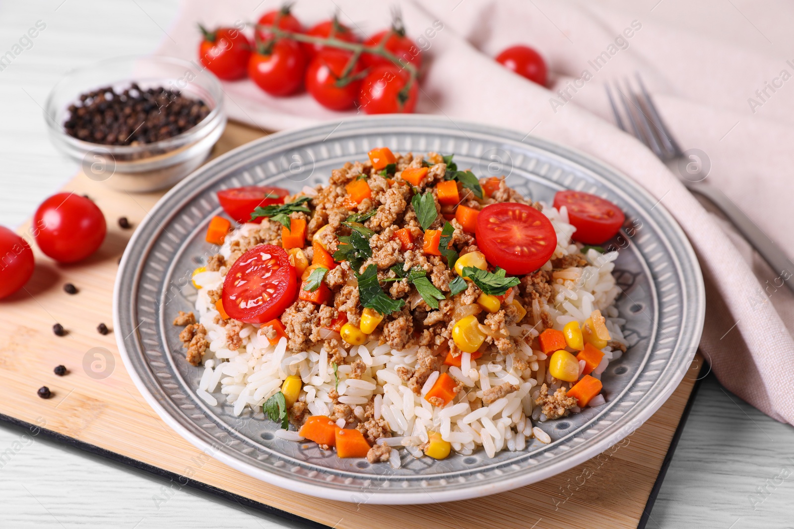 Photo of Tasty dish with fried minced meat, rice, carrot, tomatoes and corn on white wooden table, closeup