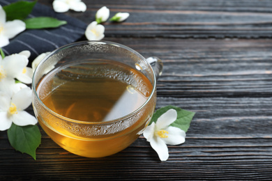 Photo of Cup of tea and fresh jasmine flowers on black wooden table. Space for text