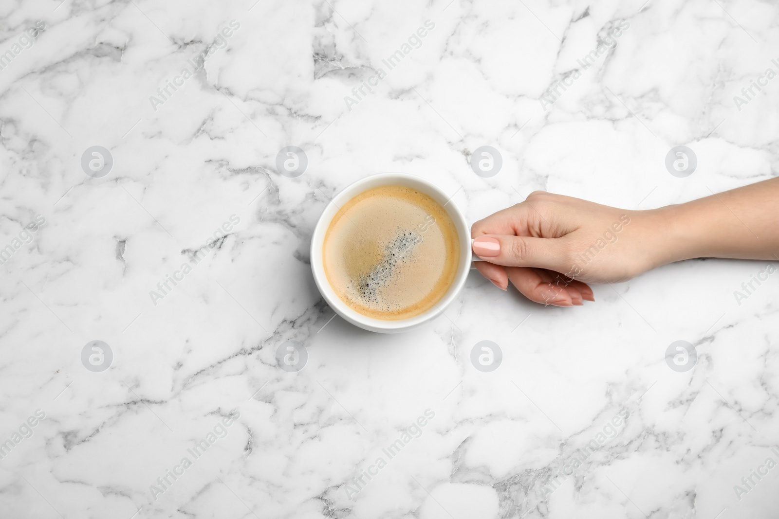 Photo of Woman with cup of coffee at white marble table, top view