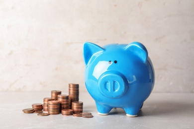 Ceramic piggy bank and many coins on table against light background. Space for text