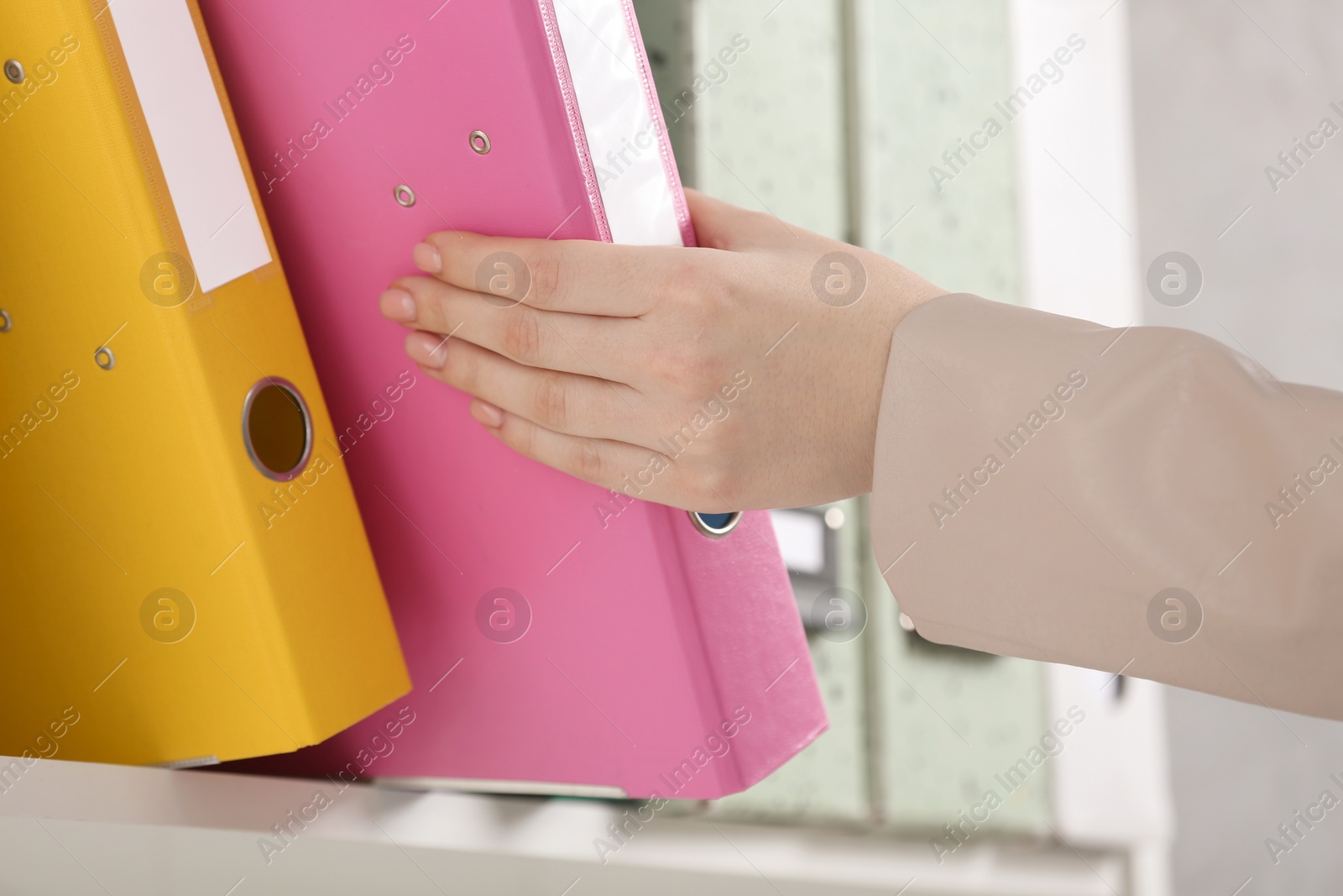 Photo of Woman taking folder with documents from shelf in office, closeup