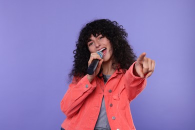 Beautiful young woman with microphone singing on purple background