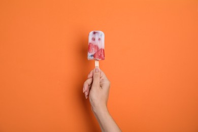 Photo of Woman holding berry popsicle on orange background, closeup