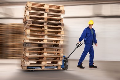 Worker moving wooden pallets with manual forklift in warehouse