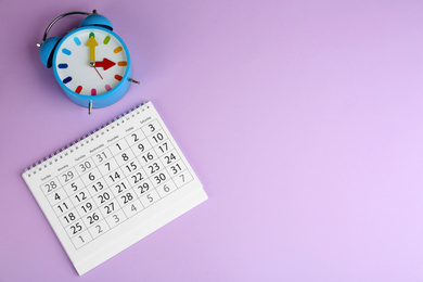 Photo of Calendar and alarm clock on violet background, flat lay. Space for text
